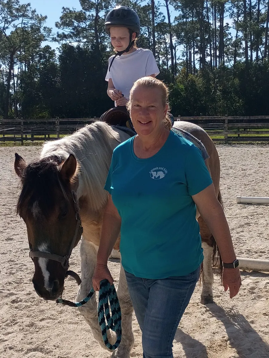 A woman walking a horse across the pasture